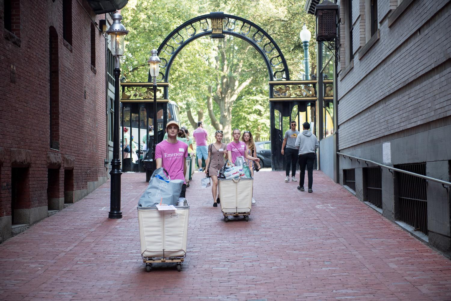 Students pushing carts on wheels down brick sidewalk.